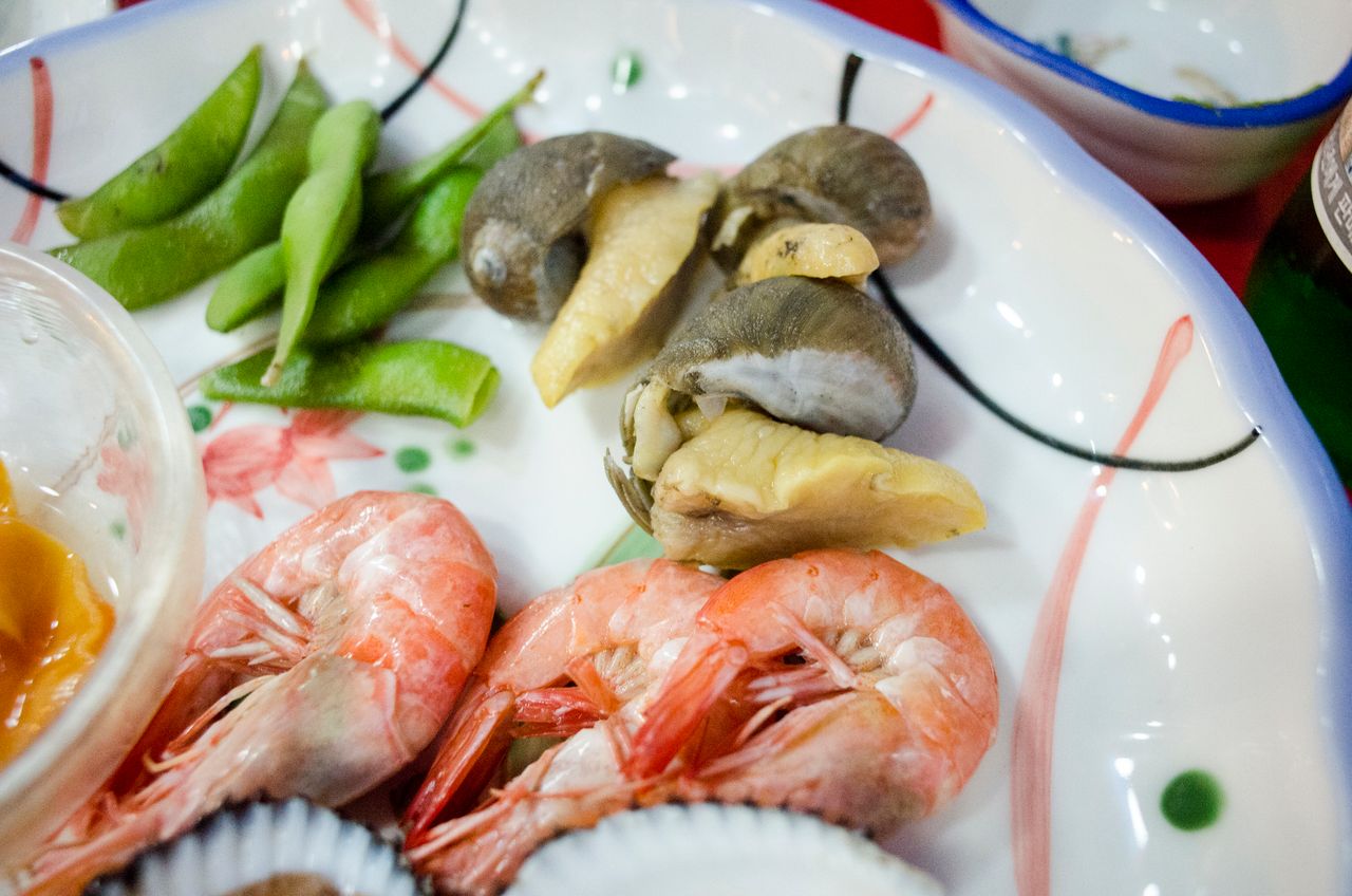 Home Appetizing seafood platter featuring shrimps, snails, and edamame beans on a decorative plate.